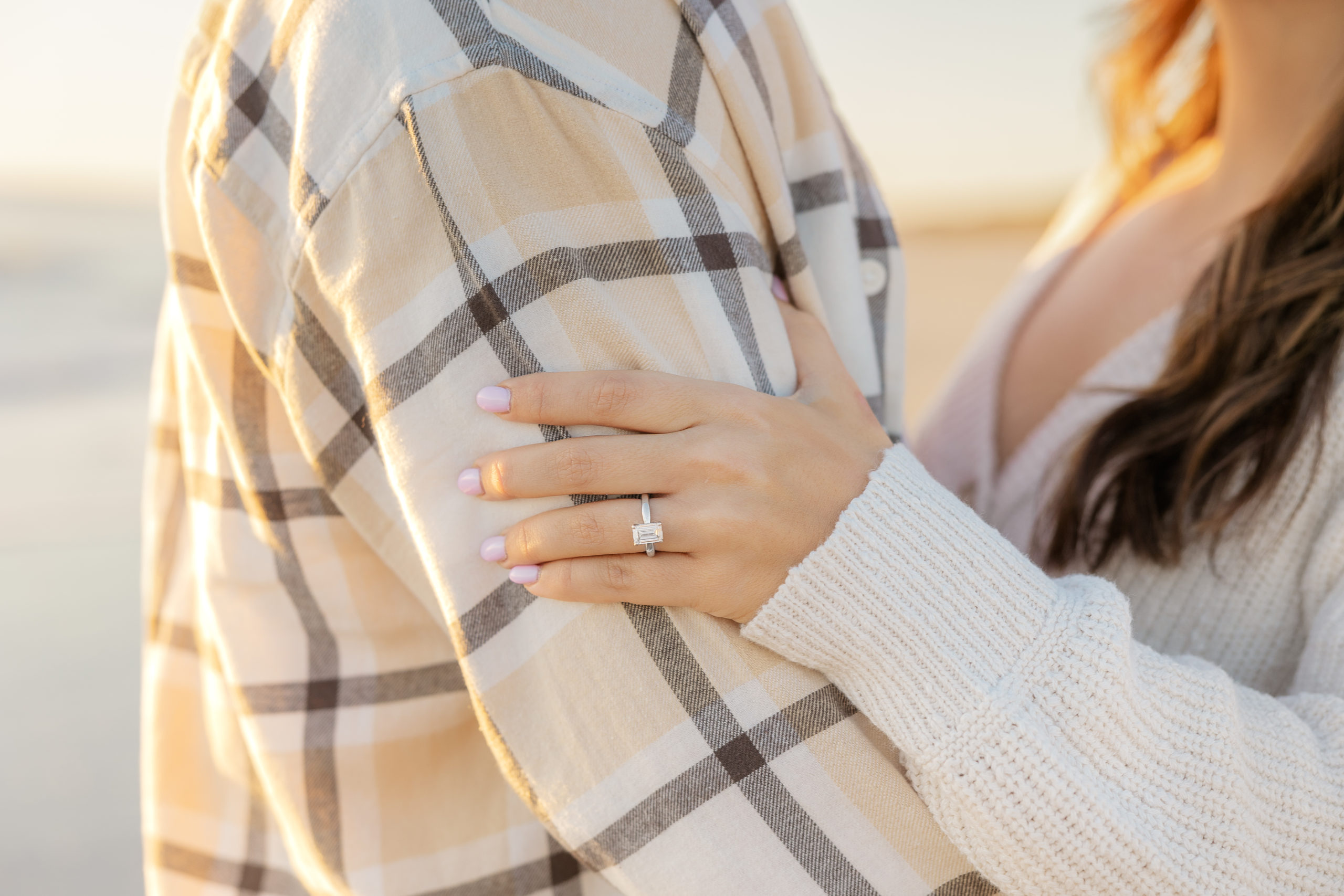couple posing on the beach with an engagement ring as the subject.