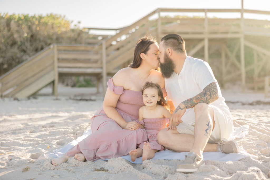 mom and dad kiss on the beach during family photo session
