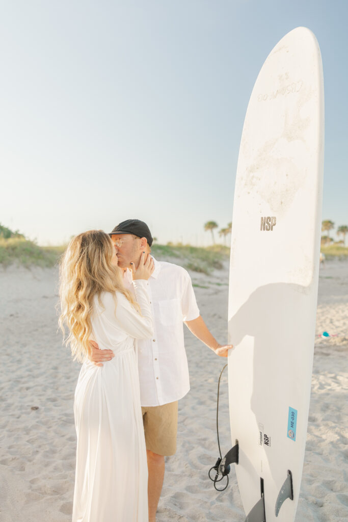 husband and wife kissing with surf board on cocoa beach