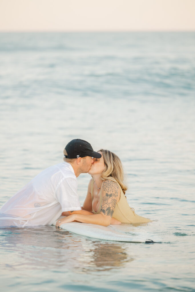 man and woman in water kissing on surf board